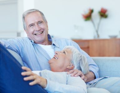 IDEAL Unfallrente: Frau und Mann lachend auf dem Sofa